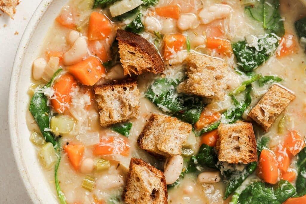 A bowl of vegetable soup with beans, carrots, celery, spinach, and croutons.