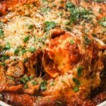 Baked ravioli being scooped out from casserole dish.