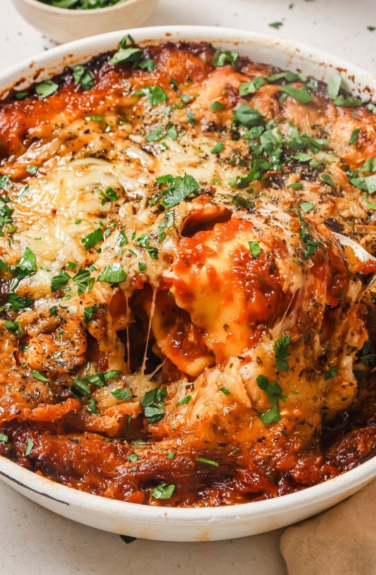 Baked ravioli being scooped out from casserole dish.