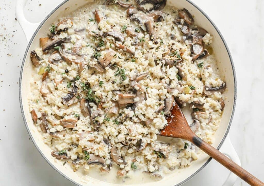 Cauliflower risotto with mushrooms in a skillet with a wooden spoon.
