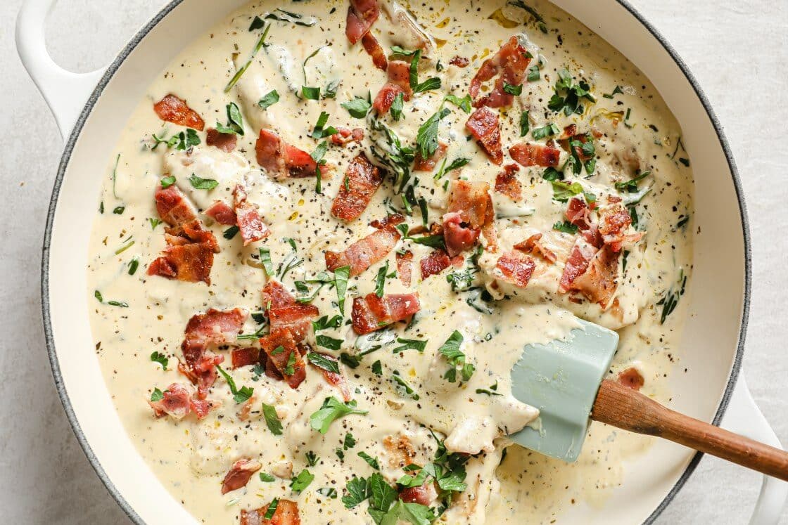 A pan of creamy dijon chicken with herbs and bacon.