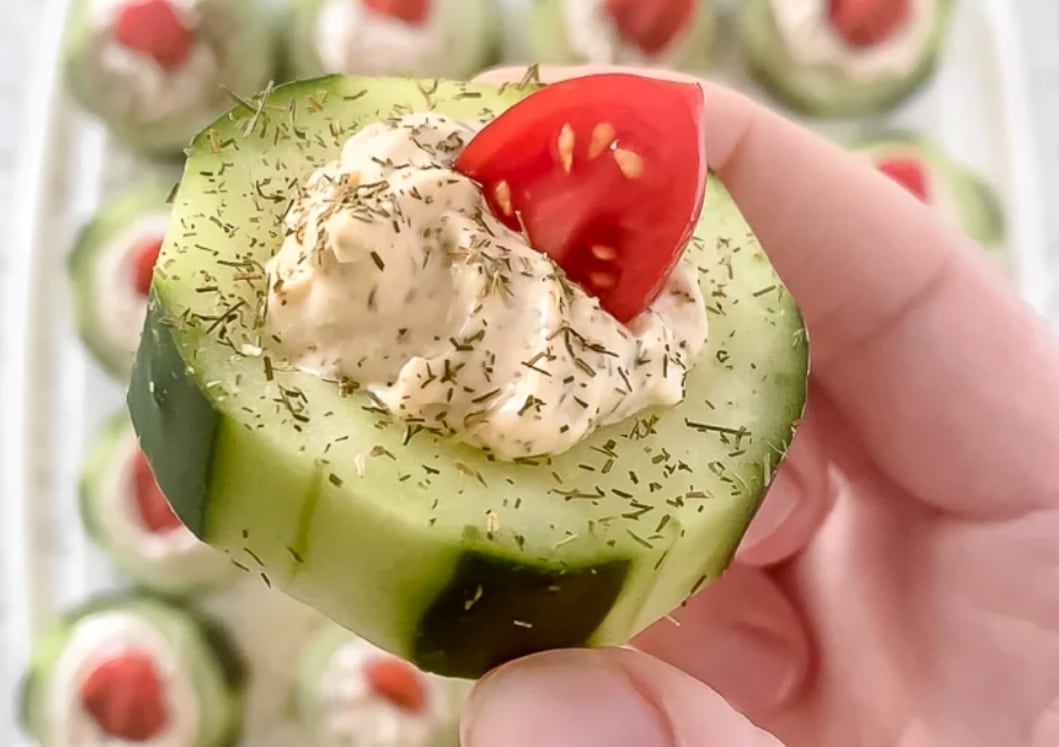 A hand holding a cucumber tomato bite.