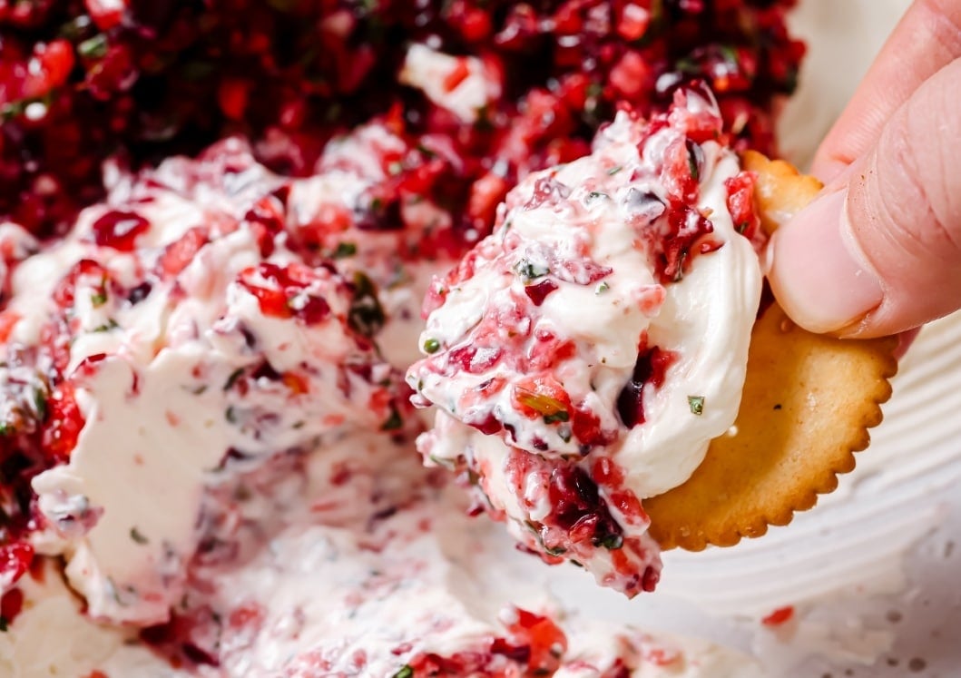 A cracker being dipped into a dish of jalapeño cranberry dip.