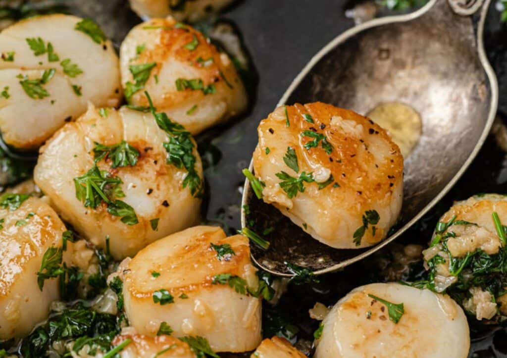 Lemon garlic scallops being served from a skillet by a spoon.