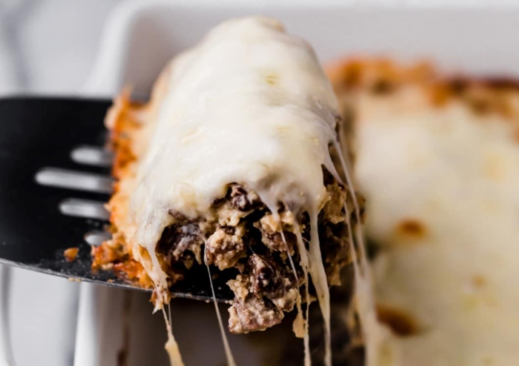 A slice of Philly cheese steak casserole being scooped from a casserole dish.