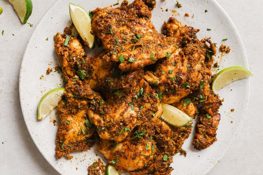 Pollo asado on a white plate with lime wedges.