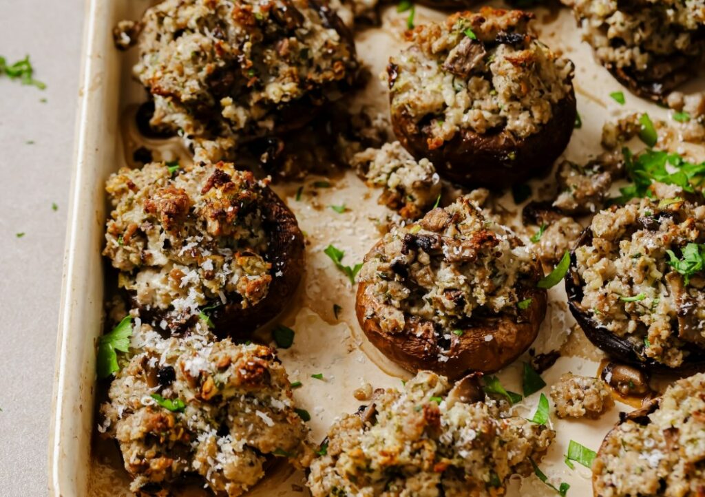 Garnished sausage stuffed mushrooms on a baking pan.
