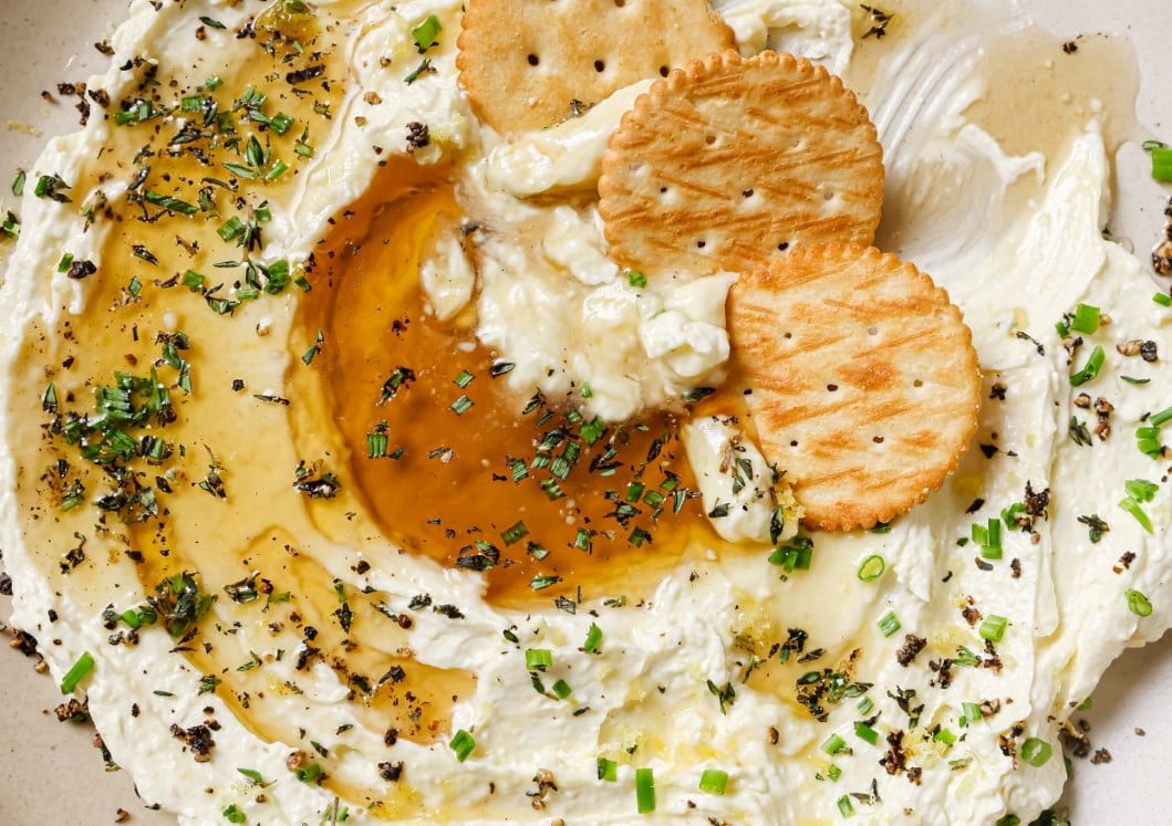 A plate of whipped feta with honey dip and crackers on it.