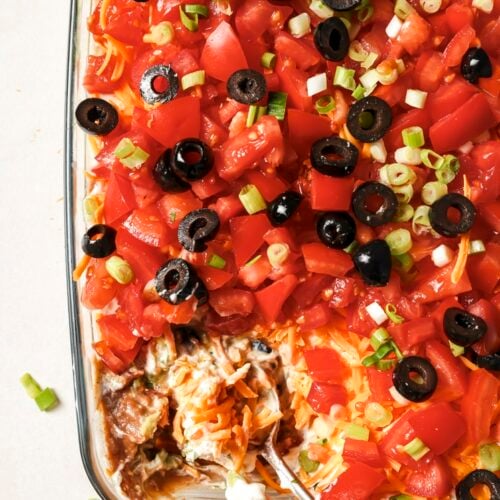 7-layer dip being scooped with a spoon in a baking dish.