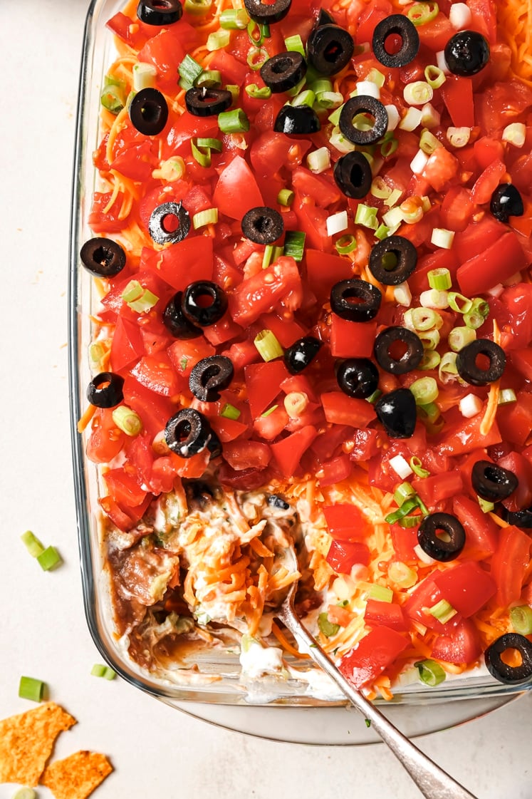 7-layer dip being scooped with a spoon in a baking dish.