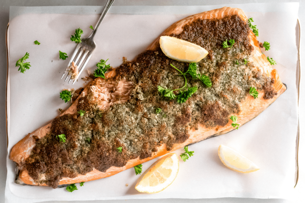 Baked Parmesan salmon with lemon slices on a parchment paper-lined baking sheet.