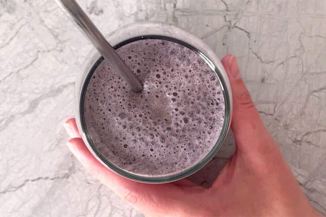 A hand holding a glass of blueberry spinach smoothie.