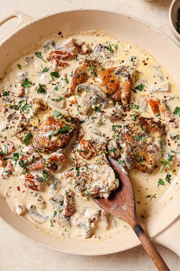 Chicken with creamy mushroom sauce in a pan with a wooden spoon.