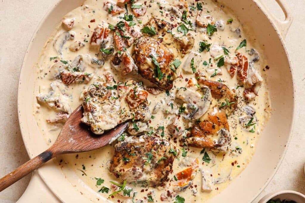 Chicken with creamy mushroom sauce in a pan with a wooden spoon.