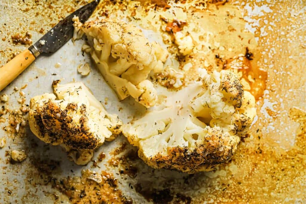 Sliced buttery roasted cauliflower on a baking sheet with a knife.