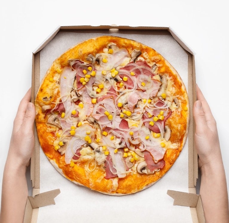 Corn kernels on pizza in a pizza box being held in two hands.