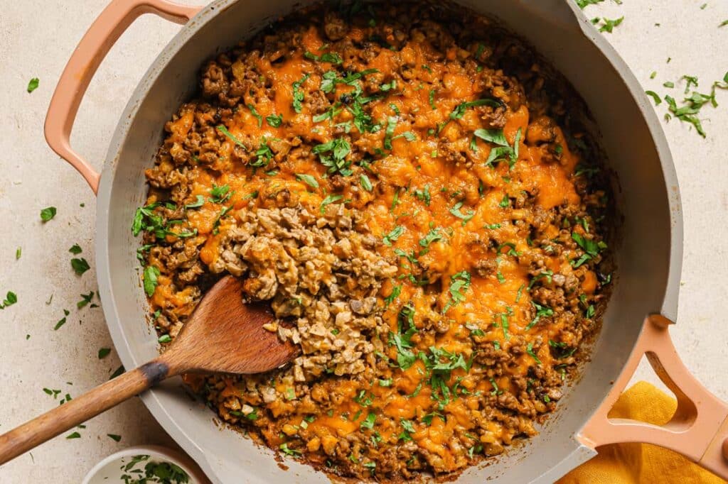Creamy ground beef skillet with cauliflower rice on a cast-iron skillet with a wooden spoon.