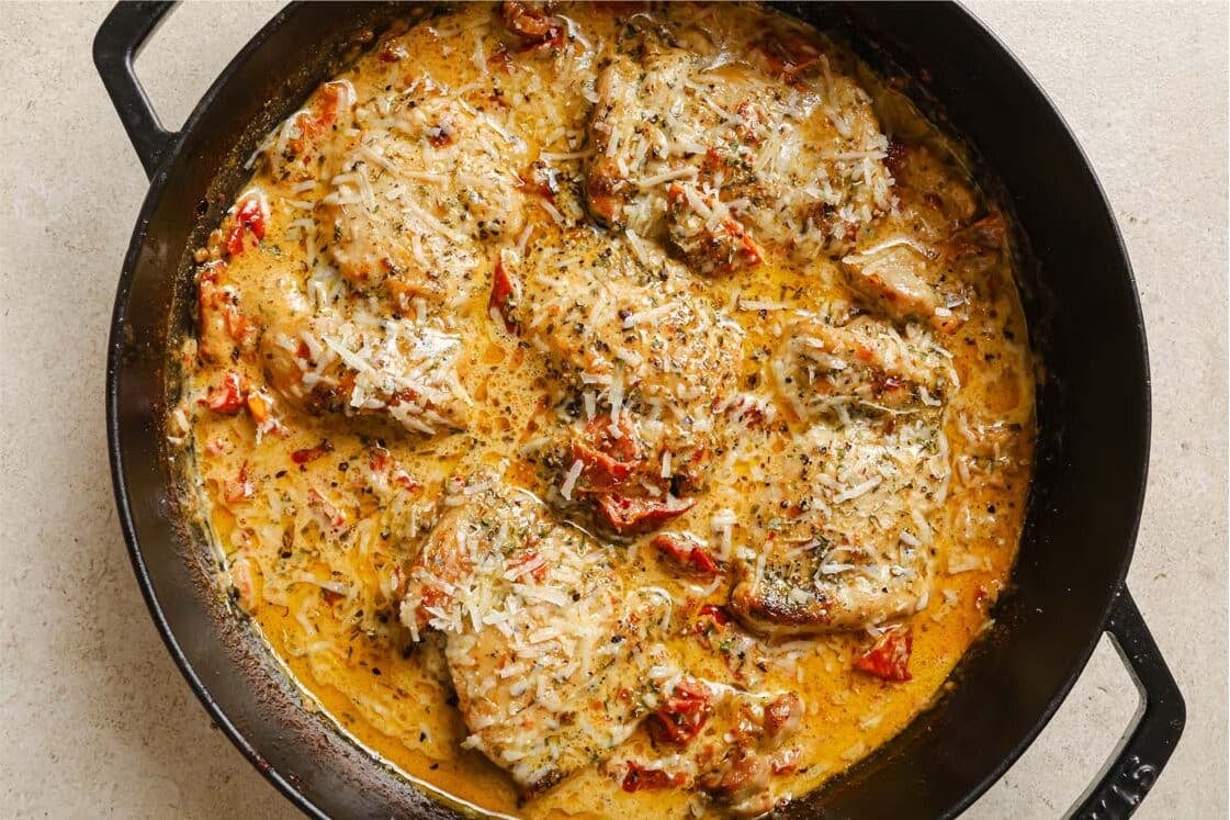 A skillet of creamy sun dried tomato chicken with a wooden spoon.