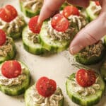 Garnished cucumber tomato bites on a plate, one held by a hand.