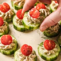 Garnished cucumber tomato bites on a plate, one held by a hand.