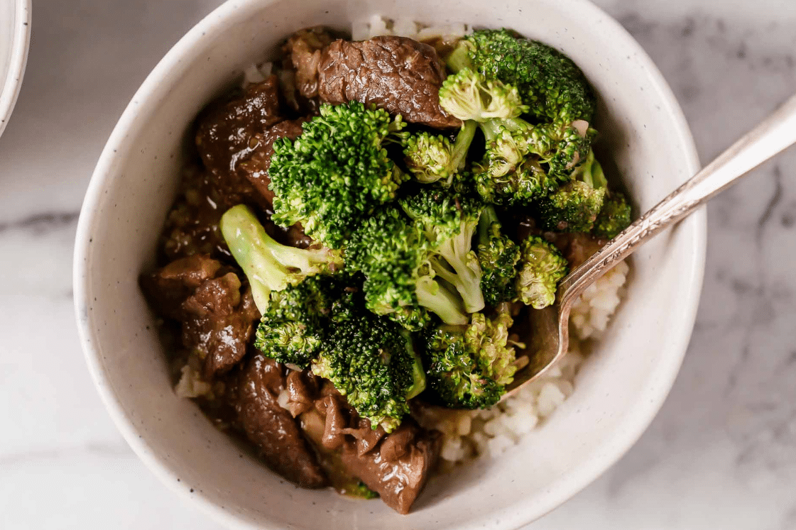 Instant Pot beef and broccoli atop white rice in a bowl with a spoon.