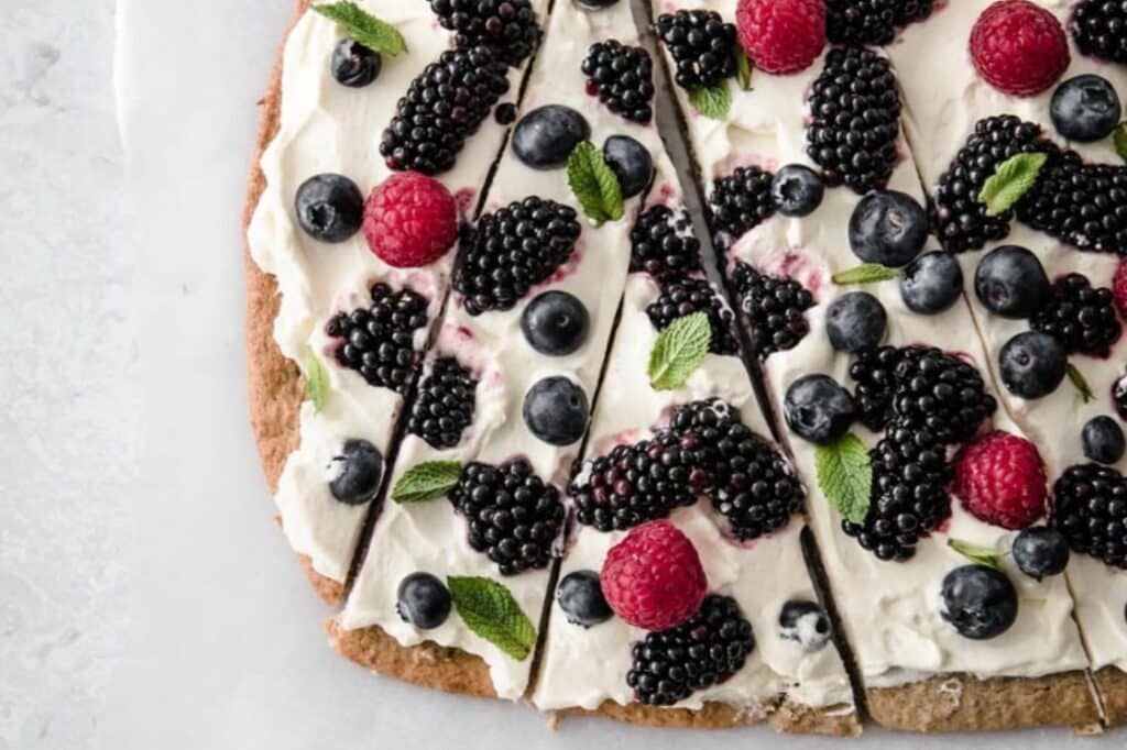 Keto gluten-free fruit pizza sliced to irregular pieces beside a small knife.