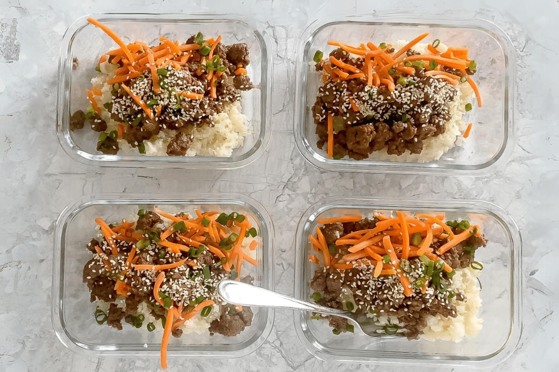 Meal prep containers with garnished Korean ground beef bowls, one with a fork.