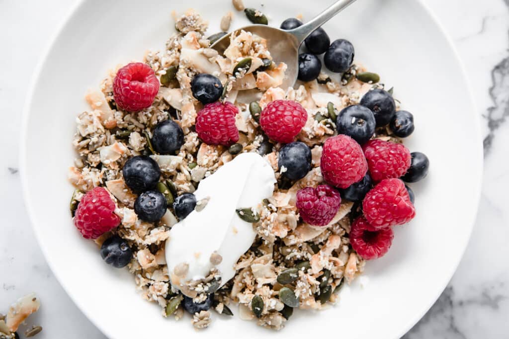 Nut-free keto cereal with yogurt and fresh fruits in a bowl with a spoon.