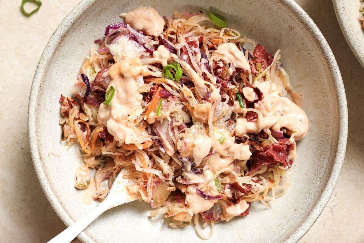 A bowl of coleslaw with creamy dressing, garnished with green onions, served in a ceramic bowl with a fork.