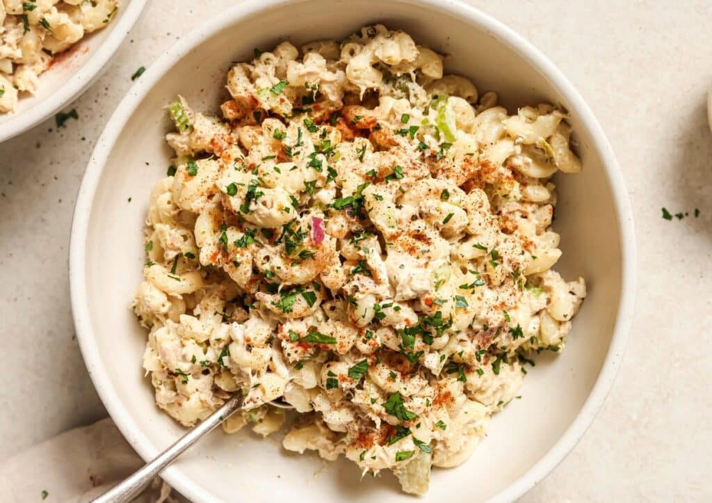 A bowl of tuna macaroni salad garnished with chopped herbs with a fork.