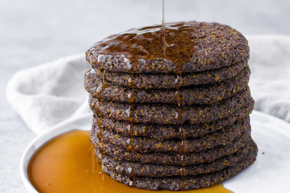 A stack of vegan keto baked pancakes driizzled with syrup on a plate.