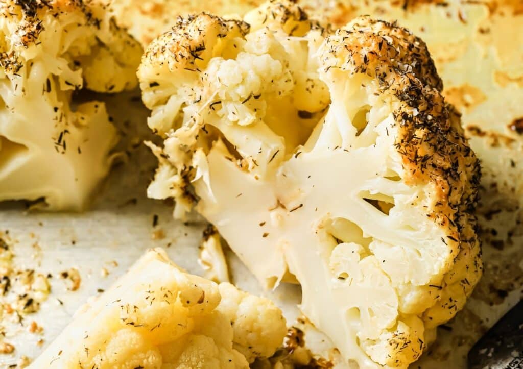 Close-up of roasted cauliflower seasoned with spices and herbs, displayed on a white surface.