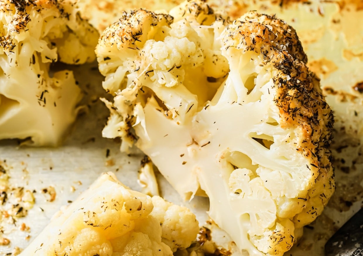 Buttery whole roasted cauliflower on a baking sheet.