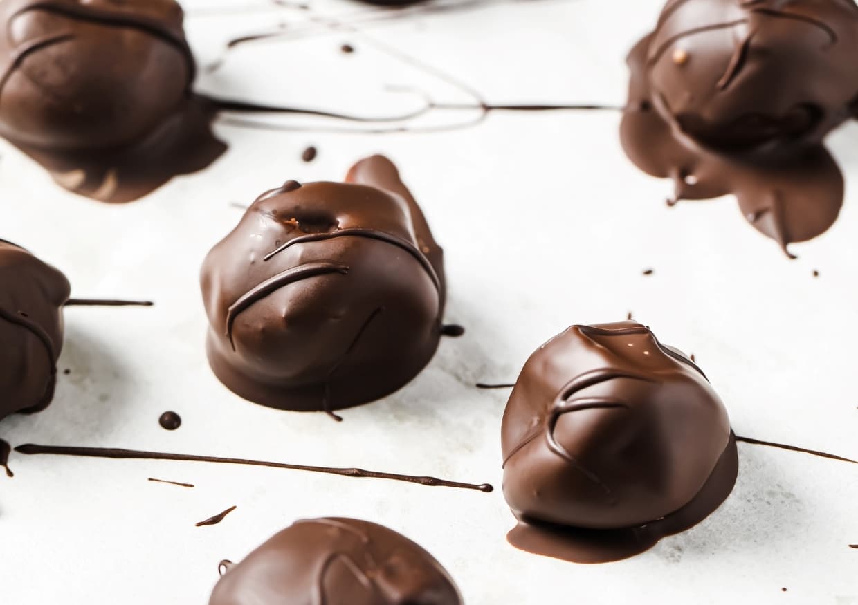 A bowl of chocolate-covered peanut butter balls with one cut in half.