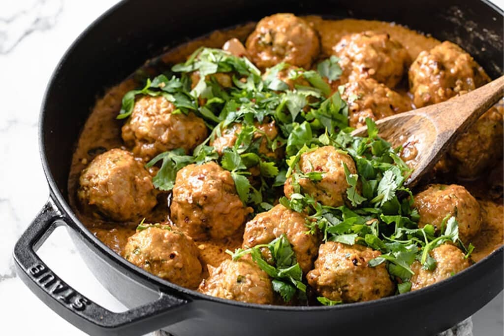 Garnished coconut curry Thai turkey meatballs in a pan with a wooden spoon.