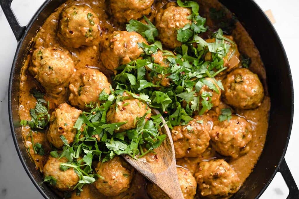 Garnished coconut curry Thai turkey meatballs in a pan with a wooden spoon.