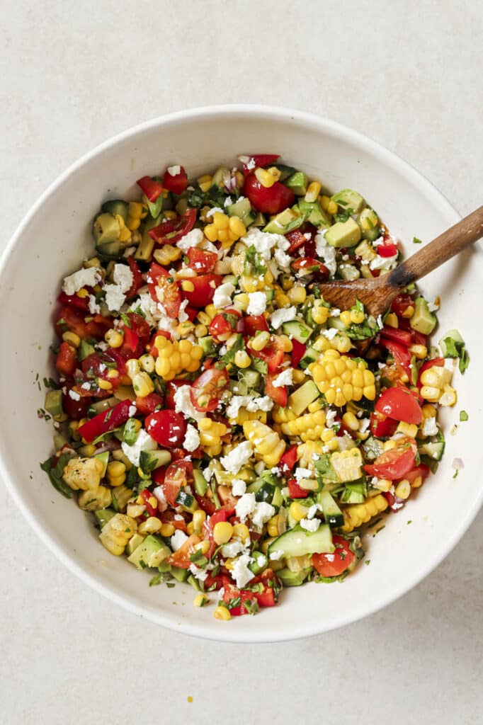 Fresh corn salad in a bowl with a wooden spoon.