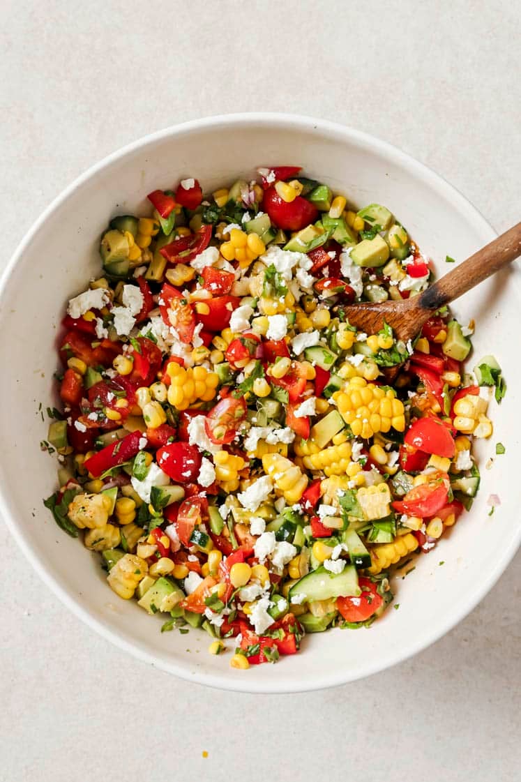 Fresh corn salad in a bowl with a wooden spoon.