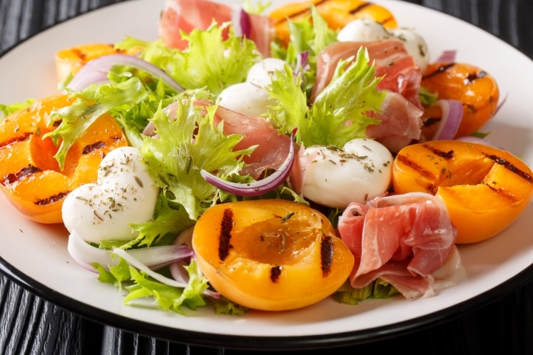Grilled apricots on a plate with cheese, lettuce, onions, and meat.