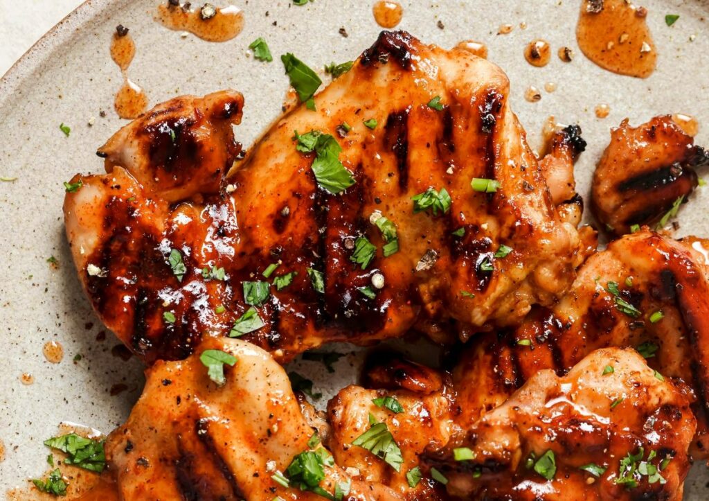 Grilled chicken pieces with a glossy glaze, garnished with chopped herbs, served on a plate.