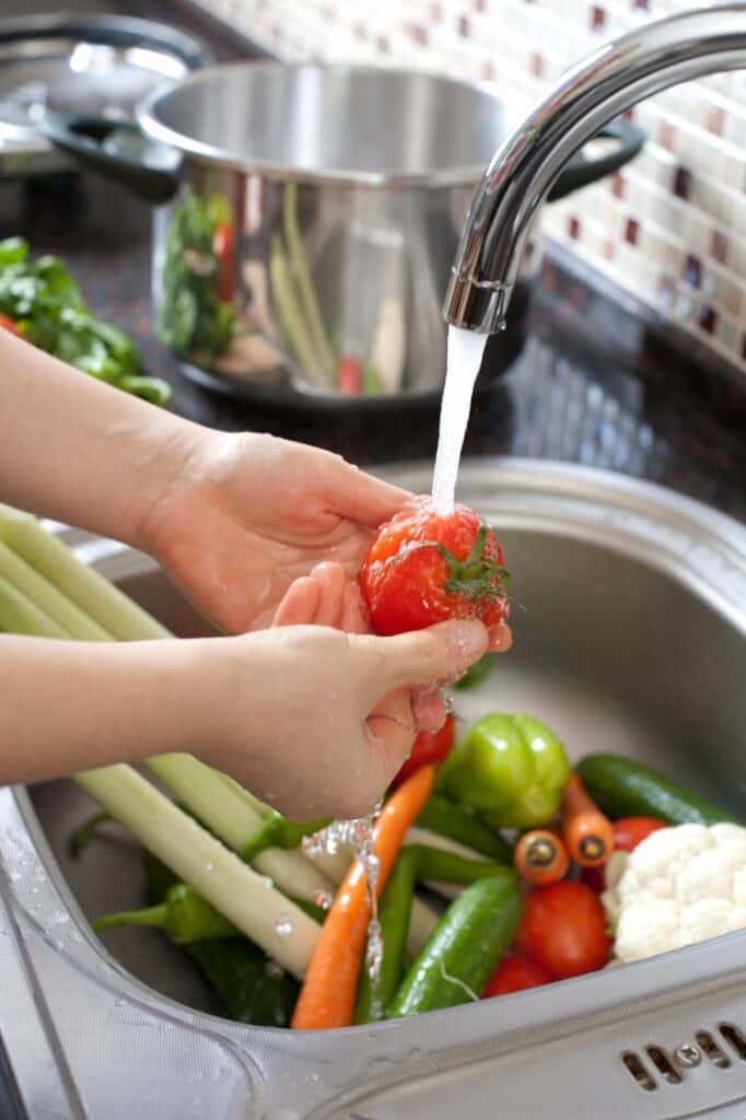 A kid washing vegetables on the sink.