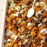 Loaded tater tots being garnished with sour cream on a sheet pan.