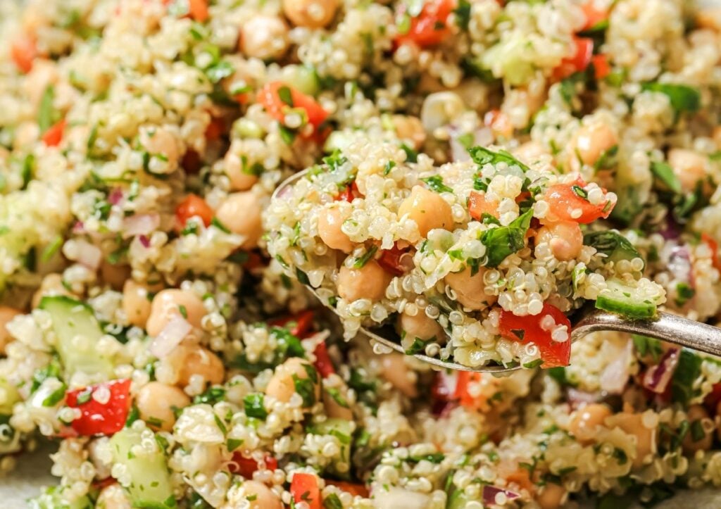 A spoonful of quinoa salad containing quinoa, chickpeas, chopped vegetables, and herbs.