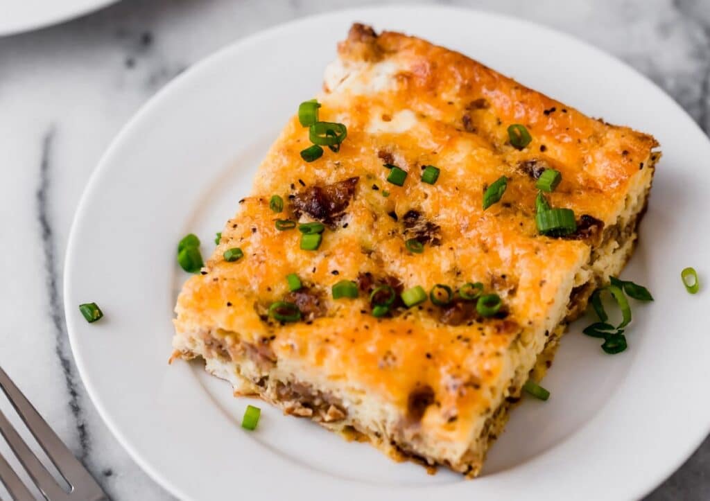 A slice of baked casserole topped with melted cheese and chopped green onions on a white plate.