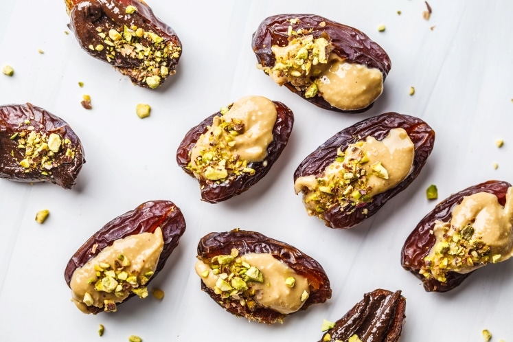 Dates stuffed with peanut butter and pistachios on a white plate.