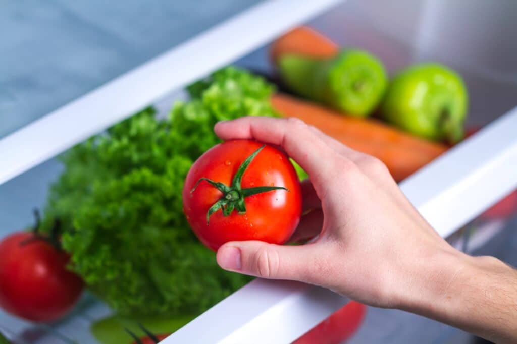 Tomato being placed in refrigerator crisper drawer.