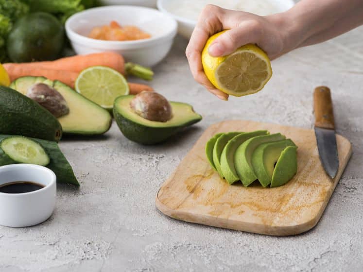 Woman squeezing lemon on cut avocado on a cutting board