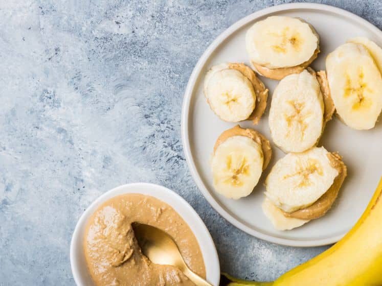 Light healthy snack made from banana slices and cashew butter on grey
