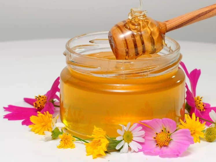 The glass jar with fresh honey on white background. Flowers on the table.