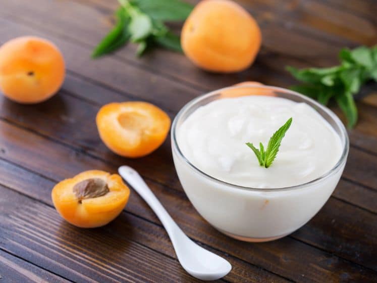 Yogurt with apricots in bowl of wooden background